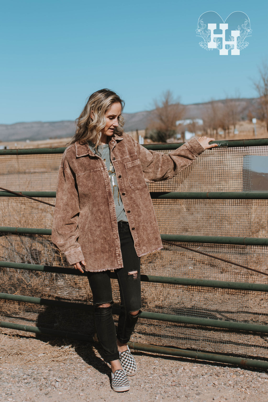 Girl standing by a fence wearing a coffee brown carduroy jacket. The brown has a light acid washed look to it. It is button up with on breast pocket on the left side. The bottom hem is unfinshed.
