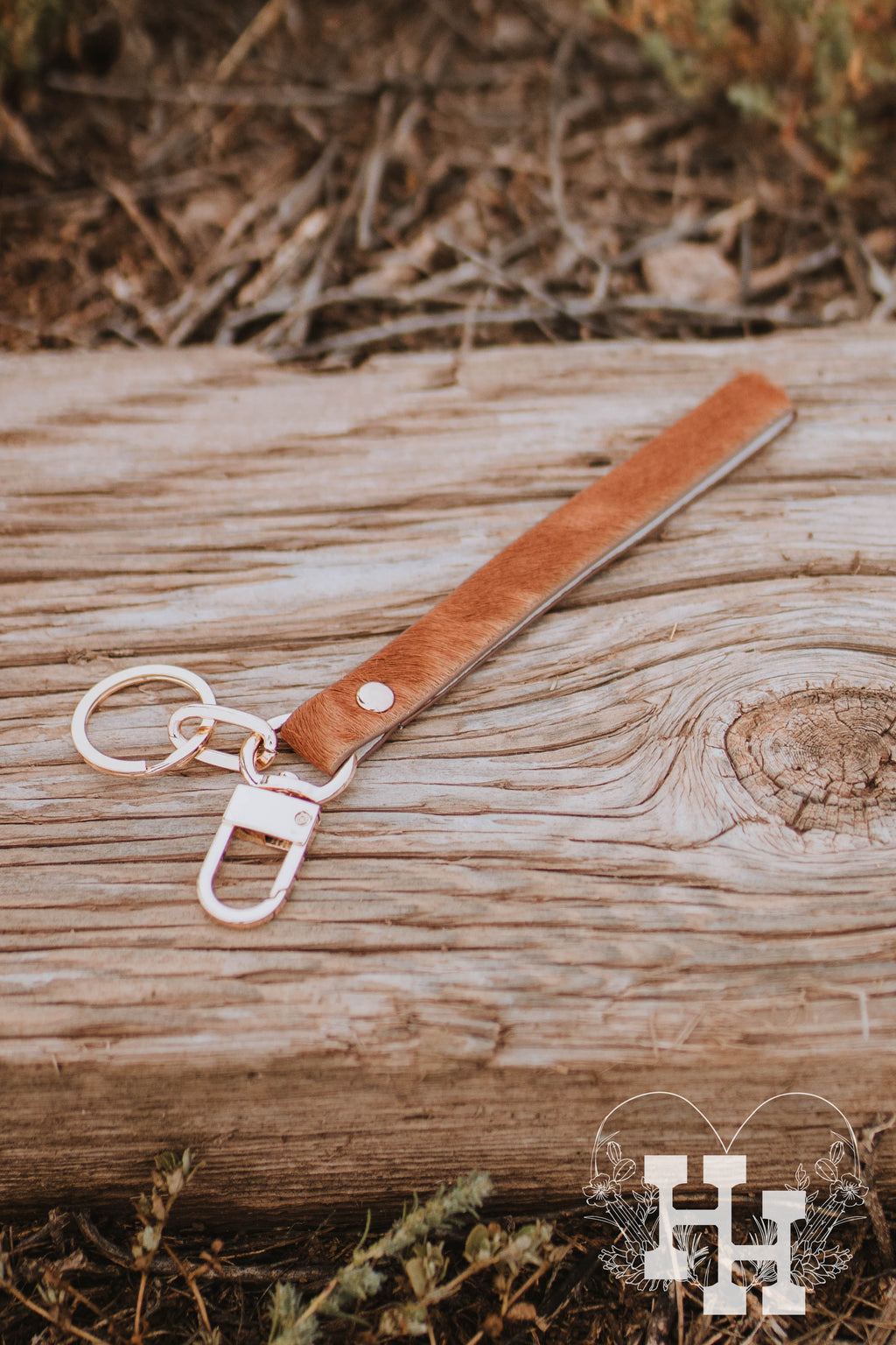 Two cow hide leather wristlet key chains with gold key ring and clip attanched. One of them is black and white spotted and the other is a red brown.