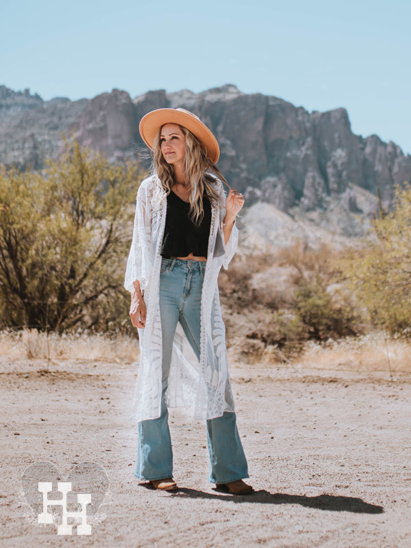 Girl stand in the desert wearing a black top with light blue flair jeans and lace duster. She is also wearing a kahki wide brim hat. 