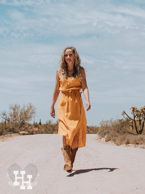 Girl walking down a dirt road wearing gloden yellow slip dress with boots.