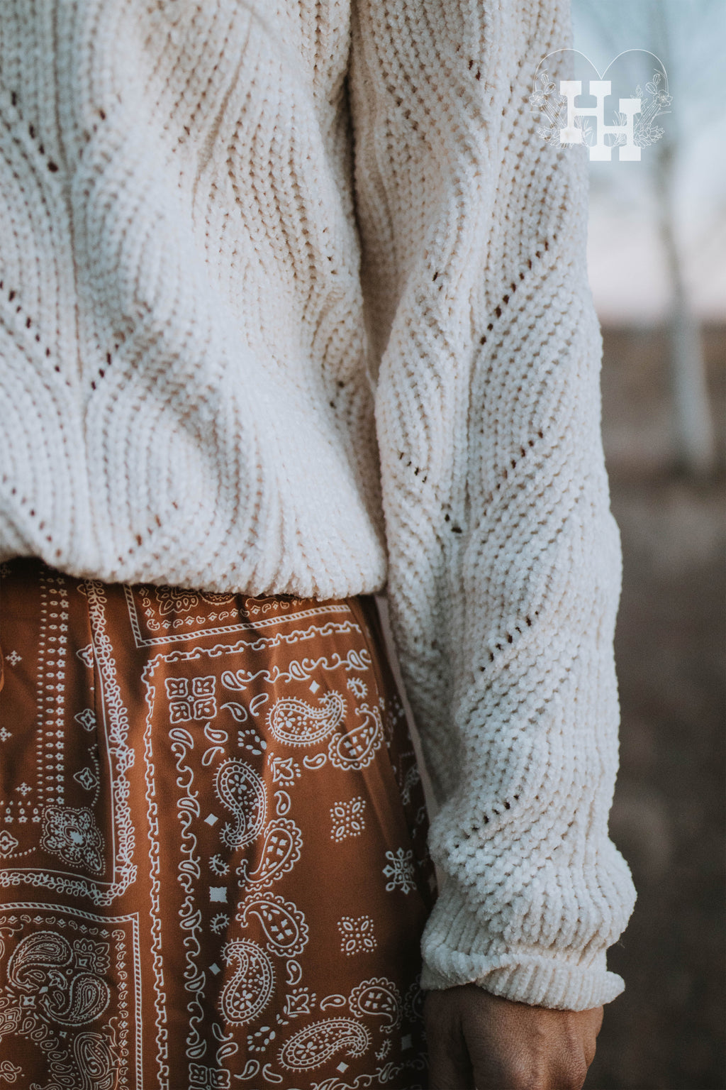 Close up of cream ivory chenille cable knit sweater and a brown bandana print skirt.