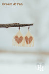 Set of dangly seed bead earings hanging on a stick on a snowy day. Earings are cream with a tan heart.