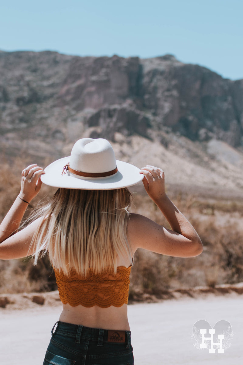 Back side of girl wearing cream colored wide brim had with a leather strap around it. She is also wearing a in dark Glolden rod and jeans.