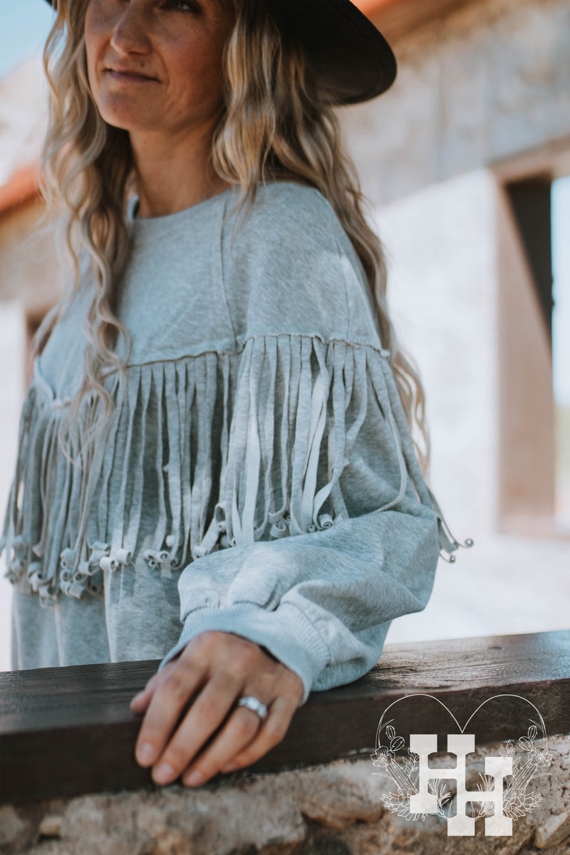 Close up of heathured gray pullover sweatshirt with long fringe detailing that wraps all the way around in a western v shape.