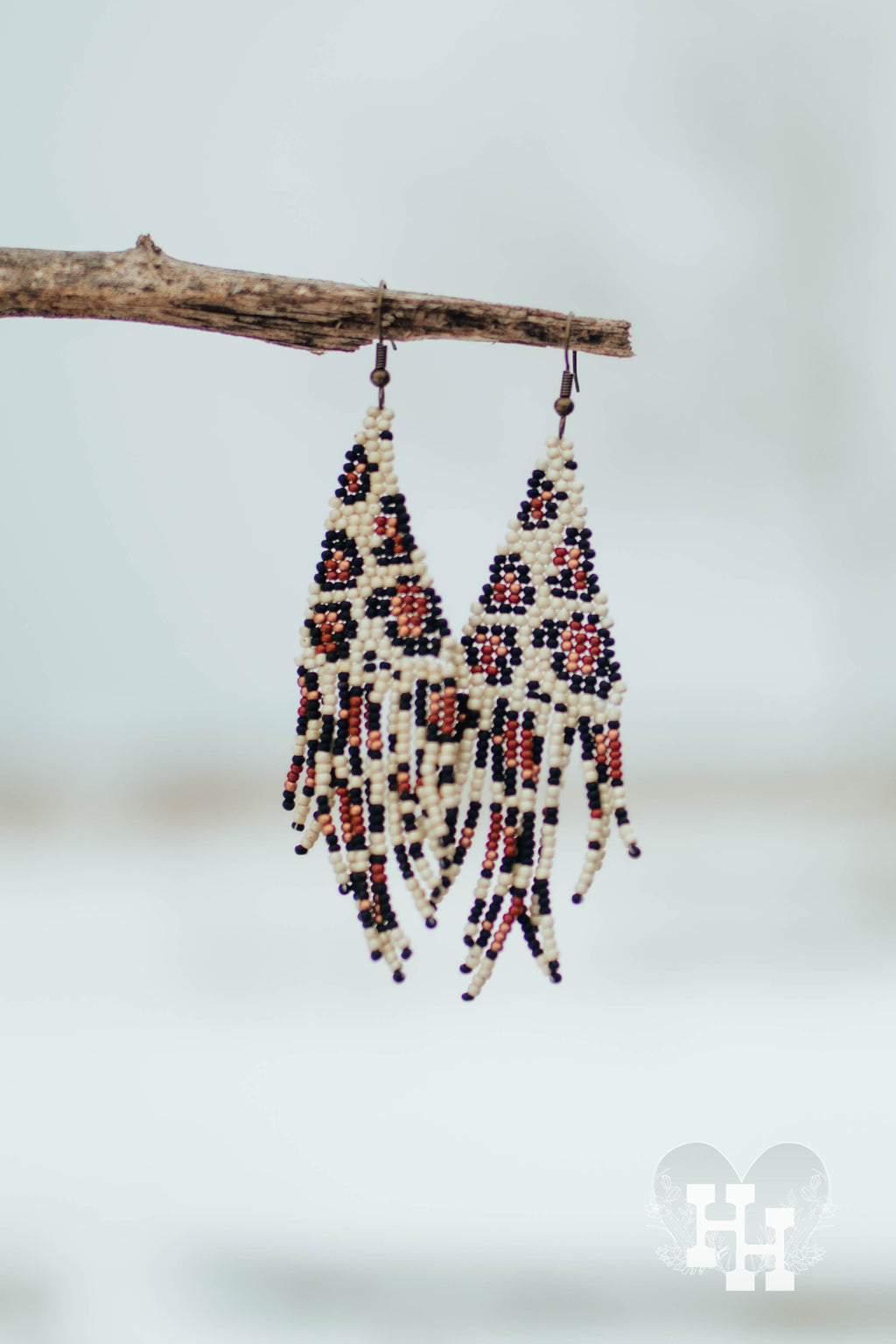 Set of dangly seed bead earrings hangon on a stick on a snowy day. Earrings are leopard patter in cream, black, brown and copper.