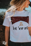 Close up of girl wearing a white tshirt that that says Let'er rip. The tshirt also has a small gold head above the saying of Rip from the Yellowstone show, then the red look of a marlboro box above that.