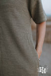 Close up of the knitted texture of a light olive green tshirt dress with hand in pocket.