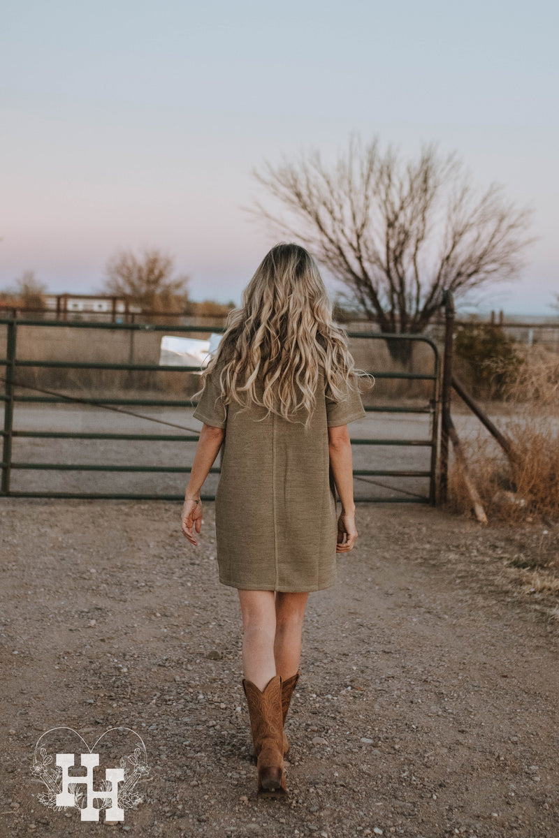 Back side of girl walking about in light olive green knit tshirt dress in boots. 