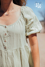 Close up of light green linen dress showing the texture, buttons down the front to the waist and puff sleeves. Dress has a scoop kneck line.