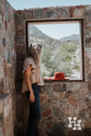 Girl standing by old window wearing Tan ruffle sleeved top and dark blue jeans. 