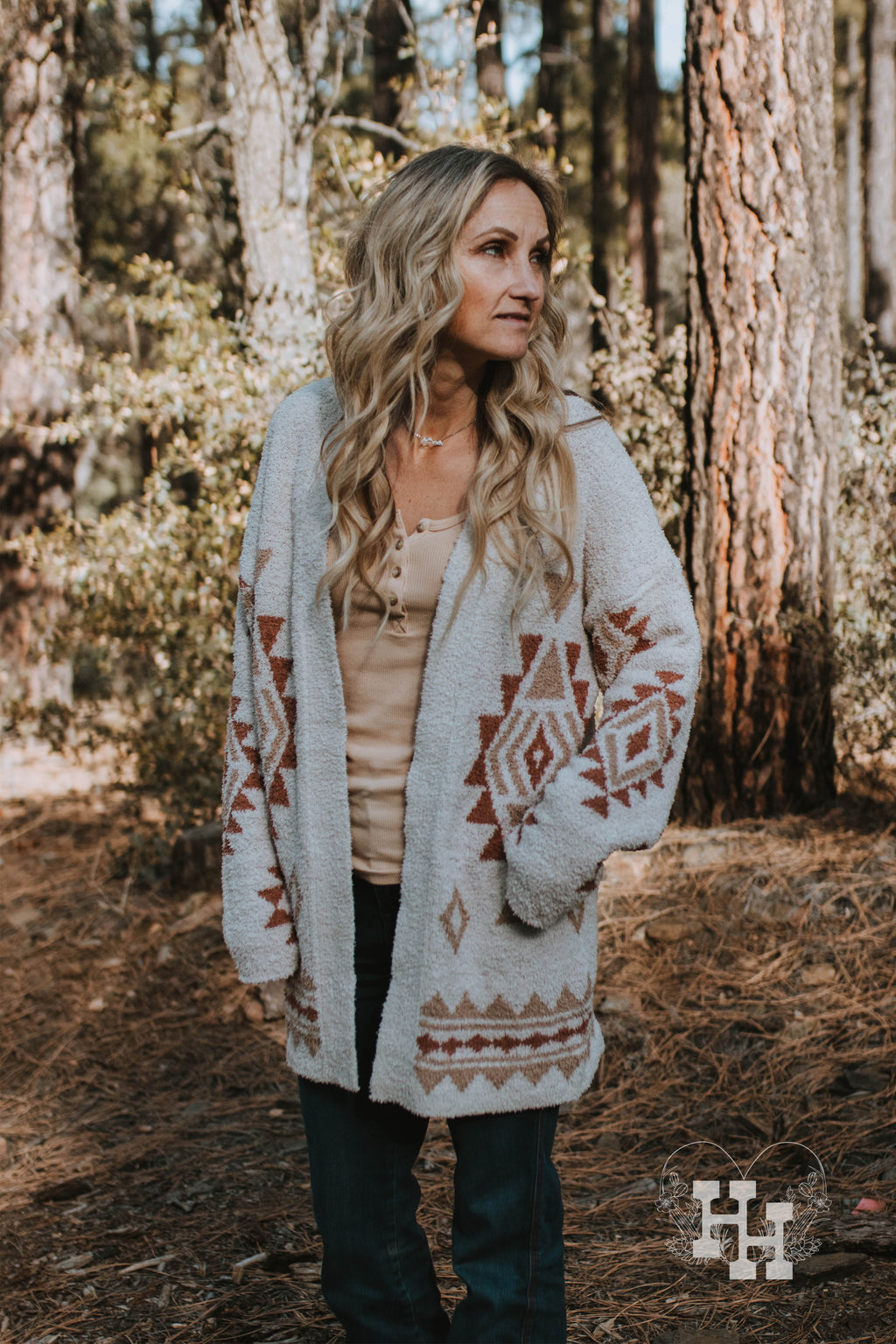 Girl wearing a long soft cardigan. The cardigan is offwhite with an aztec patern on it. The aztec pattern is a burnt orange and tan color. Cardigan lenght is about to her upper thigh. She is also wearing jeans and a tan colored tank. 