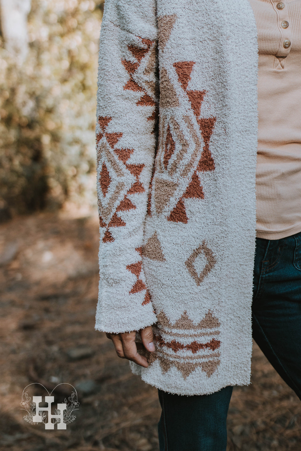 Close up of aztec sweater. Sweater is off white or ivory with an aztec print in burn orange and tan. The cardigan also has a little bit of a fuzzy texture.