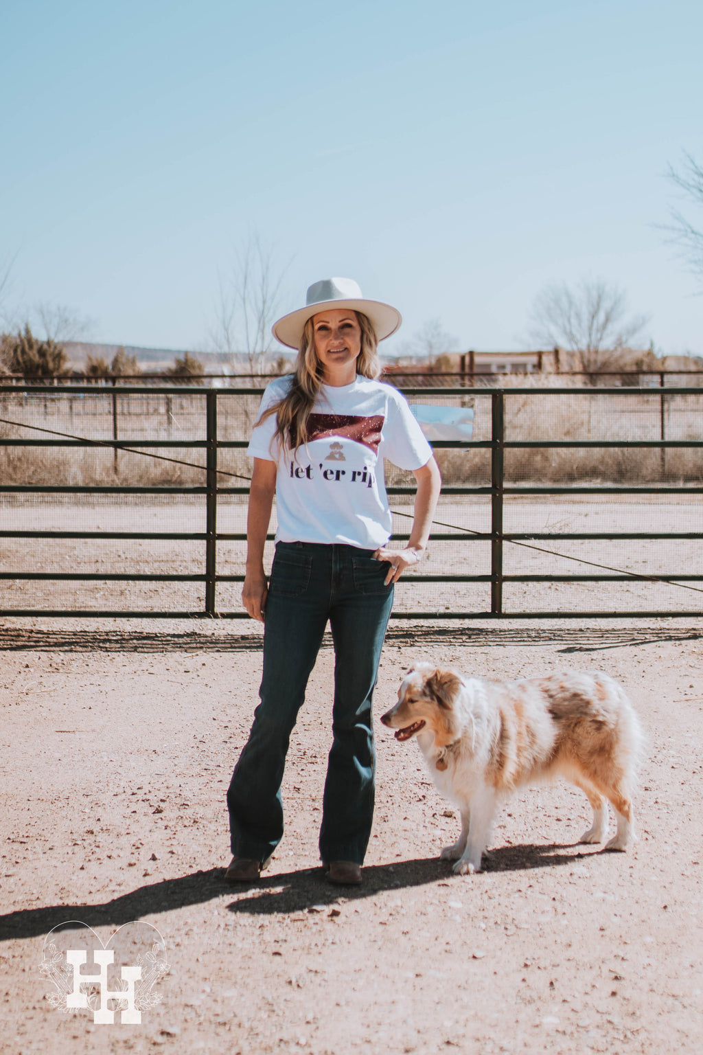 A girl standing out on a ranch with an Austrialian Sheperad standing next to her, wearing a mint green hat, jeans, and a white tshirt that that says Let'er rip. The tshirt also has a small gold head above the saying of Rip from the Yellowstone show, then the red look of a marlboro box above that.